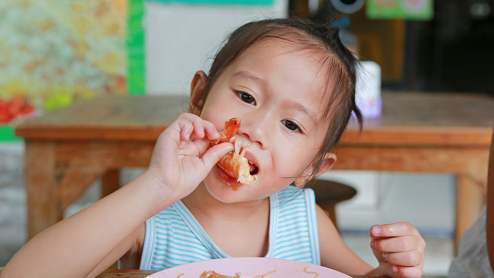 Criança japonesa comendo um camarão, um alimento que causa alergia alimentar, com as mãos