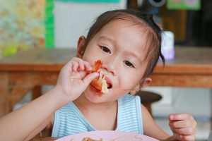 Criança japonesa comendo um camarão, um alimento que causa alergia alimentar, com as mãos